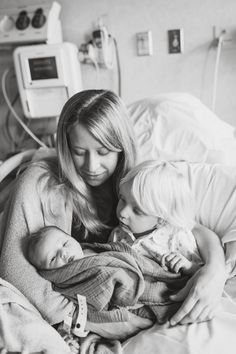 a woman holding two babies in her arms while laying on a bed with an iv machine