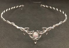 a silver bracelet with a pink stone in the center on a black cloth covered surface