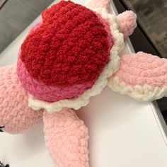 a pink stuffed animal with a red heart on it's back sitting on a table