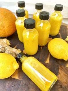 several bottles of yellow liquid sitting on top of a wooden table next to lemons and ginger