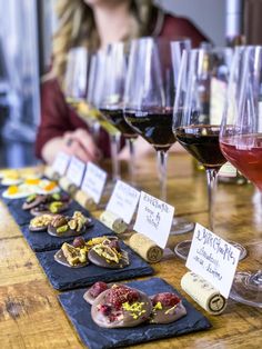 a woman sitting at a table with several glasses of wine and snacks in front of her