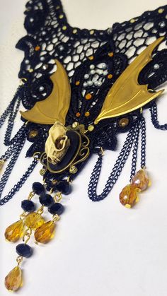 Victorian Gothic black lace collar necklace with bat skull cameo, yellow faceted crystal drops and golden bat wings, macabre cameo, Halloween jewelry Beautiful and soft macramé black lace decorated with pearl and crystal rhinestones. The bat skull cameo measures approx. 1.8x2.5 cm and is made in resin with shades and shadows brush-painted with acrylic colors. The metal frame measures approximately 3.3x3.5 cm and stands out beneath a pair of golden tone brass bat wings. Some black metal chains an Handmade Gold Gothic Choker, Gothic Gold Choker For Festivals, Gold Fantasy Jewelry For Halloween, Gothic Gold Jewelry For Halloween, Gold Skull Necklace For Halloween, Fantasy Gold Jewelry For Costume Party, Gold Fantasy Costume Jewelry, Witchy Gold Jewelry For Halloween, Black Fantasy Jewelry For Costume Party