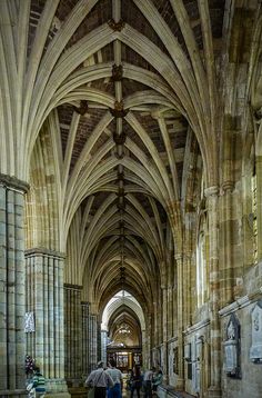 two people with umbrellas are walking in an old cathedral like building that has arches and columns