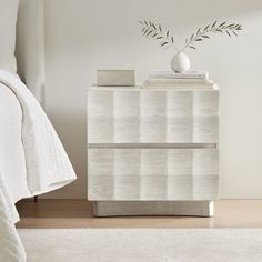 a white dresser with a vase on top of it next to a bed in a room