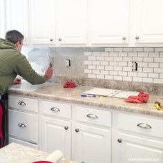 a man in a green hoodie is working on a tile backsplash with white cabinets