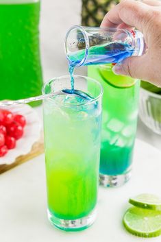 someone is pouring blue and green liquid into a glass with limes on the side