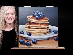 a woman standing next to a painting of pancakes and blueberries