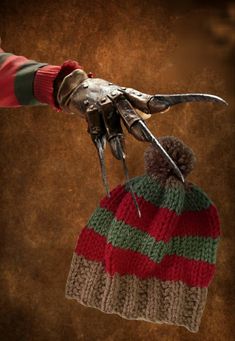 a gloved hand holding a multicolored knitted beanie with scissors attached to it