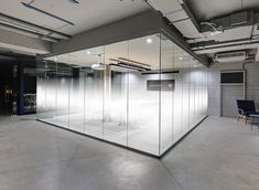 an empty room with glass partitions and chairs in the center, surrounded by concrete walls