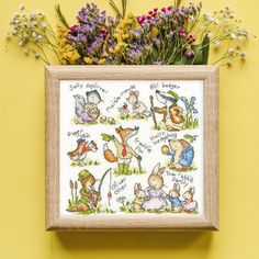 the cross stitch pattern is displayed in a wooden frame with flowers and plants around it