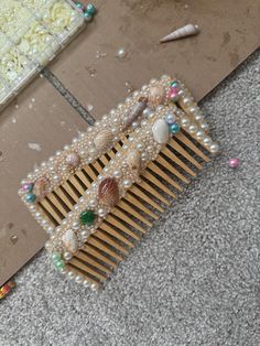 a comb with pearls and seashells on it sitting on the floor next to other items