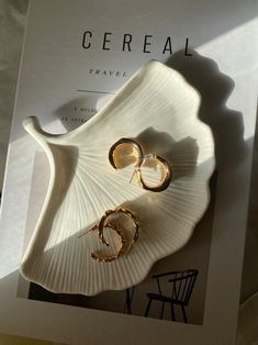 a book with two pairs of gold earrings on it next to a chair and table