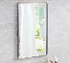 a bathroom mirror mounted to the side of a wall next to a white tiled counter