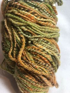 a skein of yarn is sitting on a white surface and it has green, brown, yellow and orange colors