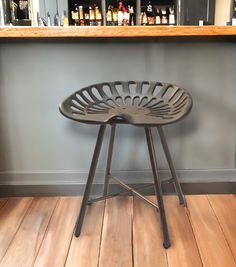 a metal stool sitting on top of a hard wood floor next to a shelf filled with bottles