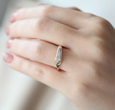 a woman's hand wearing a gold ring with an irregular shaped diamond on it