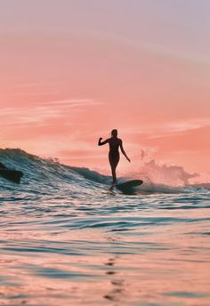 a woman riding a wave on top of a surfboard in the ocean at sunset