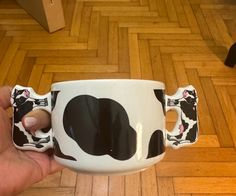 a hand holding a black and white coffee cup with a cow pattern on it's side