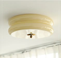 a white ceiling light hanging from the ceiling in a room with curtains on the window sill