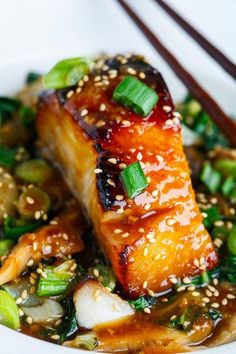 a white plate topped with meat and veggies covered in sesame seed sauce next to chopsticks