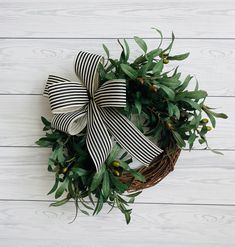 a wreath with black and white striped bow hanging on a wooden wall next to an olive branch