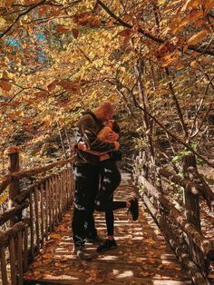 a man and woman kissing on a bridge in the woods with leaves all around them