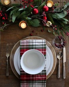 a place setting with plaid napkins, silverware and christmas greenery on the table