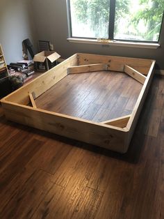 a wooden bed frame sitting on top of a hard wood floor next to a window