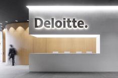 the deloitte sign is lit up in front of a white reception counter with a man walking past it