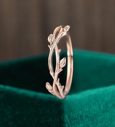 a gold ring with leaves on it sitting on a green velvet cloth in front of a wooden background