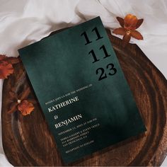 a green wedding card on top of a wooden plate next to flowers and napkins