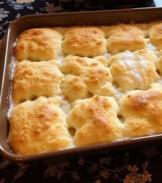 a casserole dish filled with biscuits and cheese on top of a floral table cloth