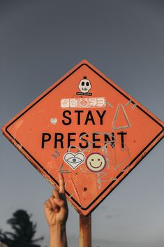 a hand pointing at an orange sign that says stay present on the side of it