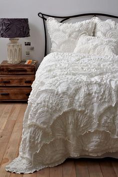 a white bed sitting on top of a wooden floor next to a nightstand and lamp