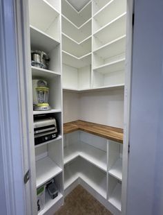 an empty pantry with white shelves and wooden counter tops, is seen in this image