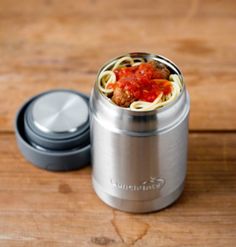 a food container with spaghetti in it sitting on a wooden table next to a green lid