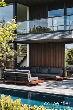 an outdoor living area with couches and tables next to a swimming pool in front of a house