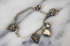 "Rare antique charm bracelet from the Victorian era. It has a variety of sterling silver puffed heart charms including a cross, grapes, and floral design. The hearts are inscribed on the back with dedications for \"Mother\" \"Edith\" and \"From Junior.\" The bracelet also has two double sided Essex crystal charms. One depicts a bust of a horse on one side, and a Scottie dog on the other. The other Essex crystal has a white dog on one side, and a Scottie dog on the other. Era: Victorian Materials Antique Charm Bracelet, Sterling Silver Charm Bracelet, Puffed Heart, Silver Charm Bracelet, Crystal Charm, White Dogs, Scottie Dog, Rare Antique, Sterling Silver Charm