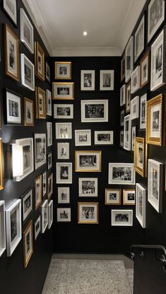 a hallway with black walls covered in pictures and gold framed frames on the wall, along with a carpeted floor