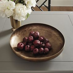 a bowl filled with plums sitting on top of a table next to white flowers