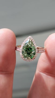 a person is holding a ring with a green stone in it's middle finger