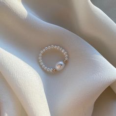 Delicate elastic fresh water pearl ring with 14kt gold filled beads. Carefully selected and high quality lustrous pearls make the ring truly beautiful and one of a kind. The delicate and minimalist design of the ring goes well with both casual and sophisticated looks. Size of the small pearl beads is approx. 2-2.5mm Size of the center large bead: 6x8mm Size of the gold filled bead: 2.5mm Follow us on INSTAGRAM: @soellejewelry Tag us on social media: #soellejewelry Packed with care and ready to s Pearl Ring Handmade, Diy Beads Ring Ideas, Pearl Beaded Ring, Ring Ideas Diy Bead, Ring Designs Beads, Silver Ring With Pearl, Elegant Adjustable Pearl Ring, Delicate Pearl Ring With Pearl Charm, White Pearl Rings With Round Beads