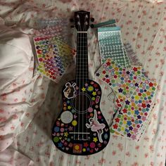 a ukulele with colorful stickers on it laying on a bed next to other items