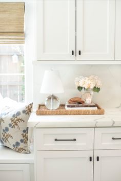 a tray with flowers on top of a kitchen counter next to a lamp and window