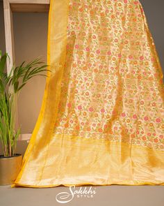 Step into regal elegance with our Yellow Gold Banarasi katan  silk saree, complemented by a beautifully stitched contrast tangerine zardozi embroidered blouse. The lustrous katan  silk, adorned with exquisite multicolored floral patterns, captures the essence of timeless tradition and modern refinement. Ideal for any special occasion, this ensemble envelops you in grace and sophistication, making you the epitome of exquisite beauty and cultural heritage. * Banarasi katan silk saree for special occasions. * Crafted from the premium quality fabric. * Supplied with a readymade blouse. * The blouse comes with an added allowance, and it can be altered to a standard size of 34"-42" on request. * Dry clean only to maintain colour and quality. Yellow Silk Traditional Wear With Resham Embroidery, Yellow Banarasi Silk Dupatta For Wedding, Yellow Meenakari Dupatta For Festivals, Gold Paithani Silk Traditional Wear For Eid, Yellow Wedding Saree With Meenakari, Yellow Meenakari Semi-stitched Saree, Semi-stitched Yellow Meenakari Saree, Yellow Banarasi Silk Dupatta With Meenakari, Semi-stitched Yellow Saree With Meenakari