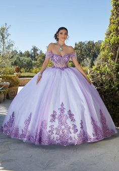 Be the epitome of quinceaera elegance in this Vizcaya by Morilee ball gown (style 89427). The sheer corset bodice offers a touch of allure, while sparkling rhinestone and crystal beaded embroidery adds a touch of glamorous shimmer. The glimmering glitter tulle skirt cascades into a grand scalloped train, featuring an elegantly embroidered hemline for a touch of timeless detail. Matching detachable off-the-shoulder sleeves complete the look, offering versatility and allowing you to customize your Qenseñera Ideas, Purple Ball Gown, Quinceañera Dresses, Sequin Ball Gown, Mary's Bridal, Tulle Balls, Iridescent Sequin, Quince Dress, Quinceanera Dress