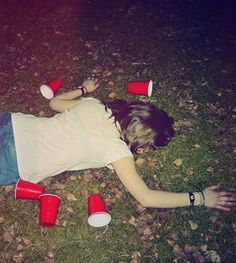 a woman laying on the ground with red cups around her head and hands in front of her body