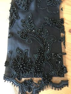 an embroidered piece of cloth with black beads and sequins on it, sitting on a wooden surface