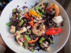 a white bowl filled with rice, shrimp and veggies next to a red pepper