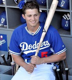 a baseball player sitting in the dugout with his bat on his shoulder and smiling at the camera